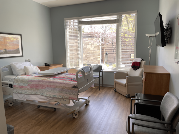 Hospice Residence empty bed in room with large window and chairs